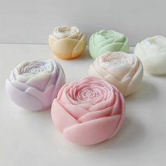 four soaps with different colors and designs on white surface, including one pink rose