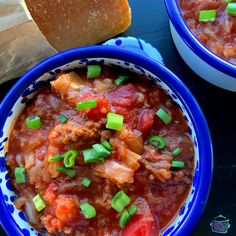 two bowls filled with meat and vegetables next to a loaf of bread on a table