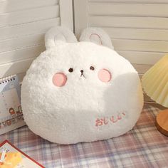 a white stuffed animal sitting on top of a table next to a book and lamp