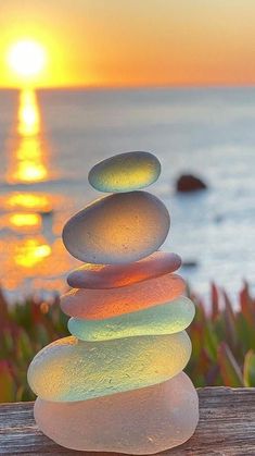 a stack of rocks sitting on top of a wooden table next to the ocean at sunset