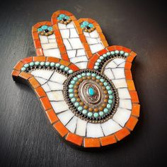 an orange and white hamsa hanging on a black table with beads around the edges