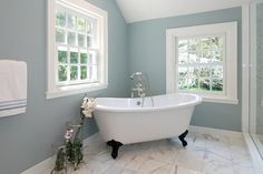 a white bath tub sitting under two windows in a bathroom