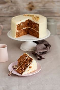 a slice of carrot cake with white frosting on a plate next to a cup