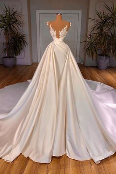 a white wedding dress on display in front of a wooden floor with potted plants