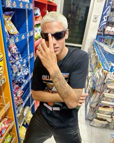 a man with tattoos on his arm standing in front of a store shelf and holding his hand up to his face