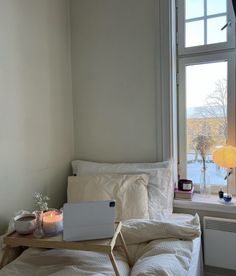 a laptop computer sitting on top of a wooden table next to a bed with white sheets