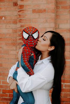 a woman kissing a stuffed spider man in front of a brick wall