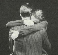 two people hugging each other in front of a black background