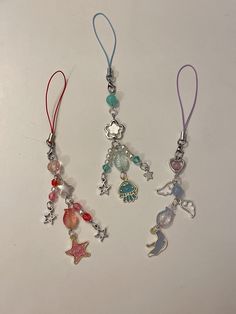 three necklaces with charms attached to them on a white surface, one has a star and the other is a mermaid