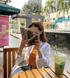 a woman sitting at a table with a book in front of her and a drink