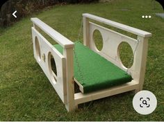 a wooden bench with a green cushion on the seat and chain attached to it, sitting in grass