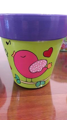 a green cup with a purple lid and a bird design on the side sitting on a wooden table