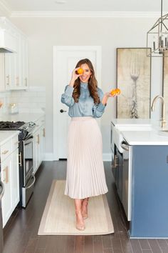 a woman standing in a kitchen holding two oranges