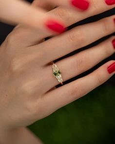 a woman's hand with red nail polish holding a gold and green diamond ring