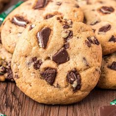 three chocolate chip cookies sitting on top of a wooden table next to candy bar wrappers