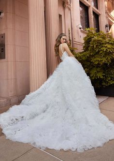 a woman in a white wedding dress standing on the side of a building with her back to the camera