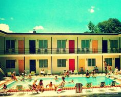 people are sitting in chairs around the pool outside an apartment building with colorful shutters and balconies