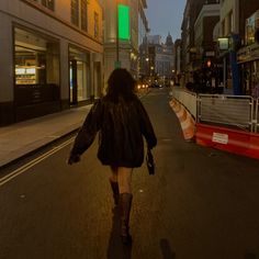 a woman is walking down the street at night with her back turned to the camera