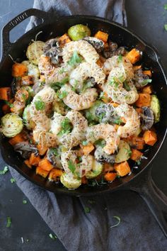 a skillet filled with vegetables and cheese on top of a gray cloth next to a spoon