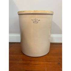 a white pot sitting on top of a hard wood floor next to a wall with a crown drawn on it