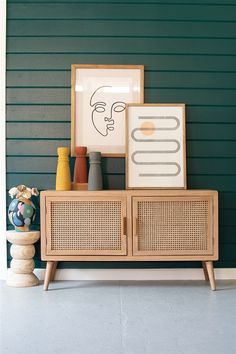 a wooden cabinet sitting in front of a green wall next to vases and pictures