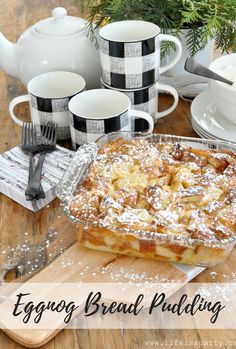 an eggnog bread pudding sitting on top of a wooden table next to cups and saucers