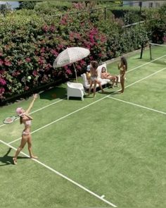 two women in bikinis playing tennis on a grass court with pink flowers behind them