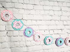 doughnuts are hanging on a string in front of a white brick wall with pink, blue and green donuts