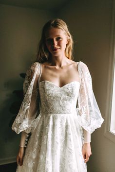 a woman wearing a white dress standing in front of a window