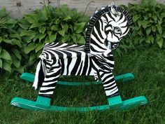 a toy zebra sitting on top of a green rocking horse in the middle of some grass