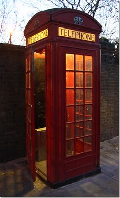 a red phone booth sitting on the side of a road next to a brick wall