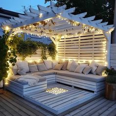 an outdoor seating area is lit up with string lights and white pillows on the couches