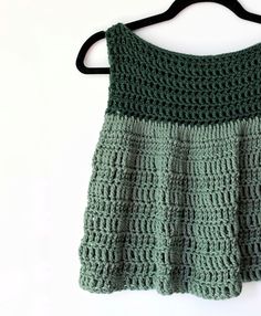 a green crocheted top hanging on a black hanger against a white wall