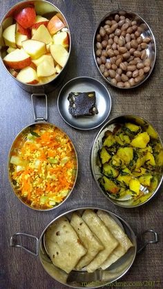 four metal pans filled with food on top of a wooden table next to beans and apples