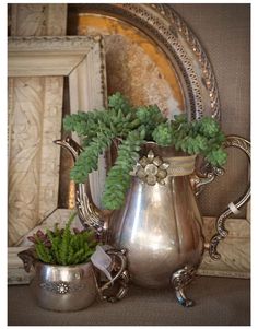 two silver vases with plants in them sitting on a table next to a mirror