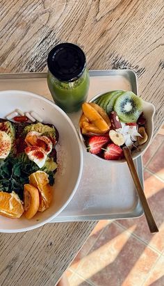 there is a bowl of fruit on the tray next to a glass of green juice