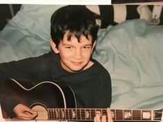 a young boy is holding an acoustic guitar