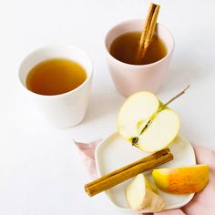 two cups of tea, cinnamon sticks and apples on a white plate with pink napkins