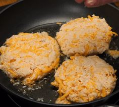 three hamburger patties are being cooked in a skillet on the stove with grated cheese