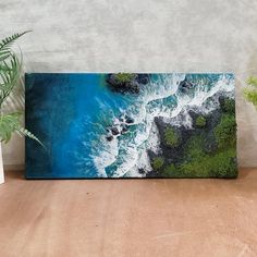 an aerial view of the ocean with waves crashing on rocks and green trees in the foreground