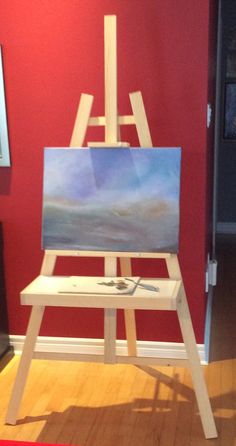 an easel sitting on top of a hard wood floor next to a red wall