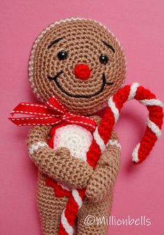 a crocheted gingerbread man holding a candy cane on a pink background,