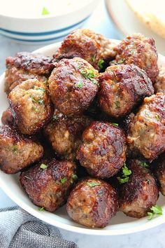 a white bowl filled with meatballs and garnished with parsley on top