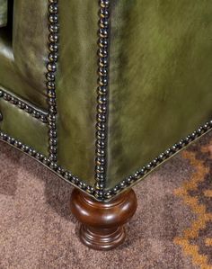 an upholstered green leather chair with studded trimmings and wooden legs