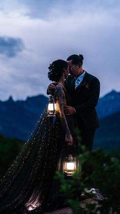 a bride and groom standing next to each other in front of mountains with lights on them