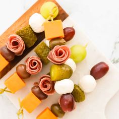 several different types of food are arranged on a white platter with grapes, cheese and crackers