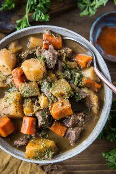 a bowl of stew with carrots, potatoes and parsley in it on a wooden table