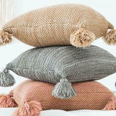 three pillows stacked on top of each other with tasselled pom poms