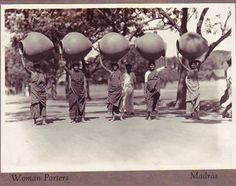 an old black and white photo shows men carrying large objects on their heads, with trees in the background