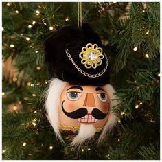 a christmas ornament hanging from a tree with lights in the background and an image of a man's face painted on it